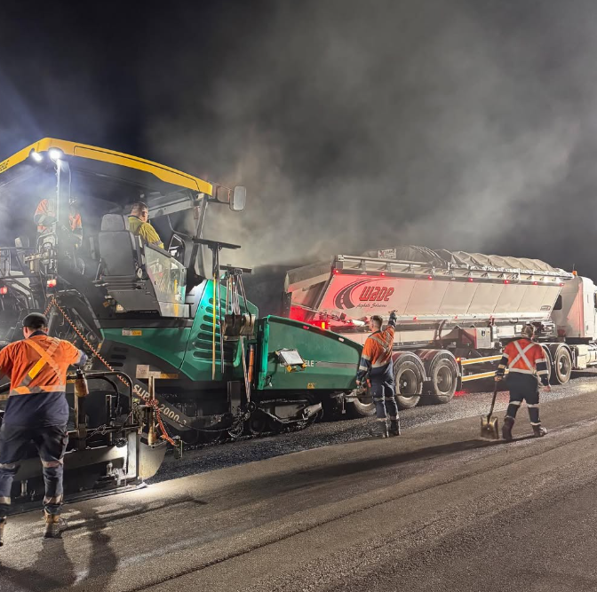 Asphalt paving crew working beside a paver and Wade-branded truck at night